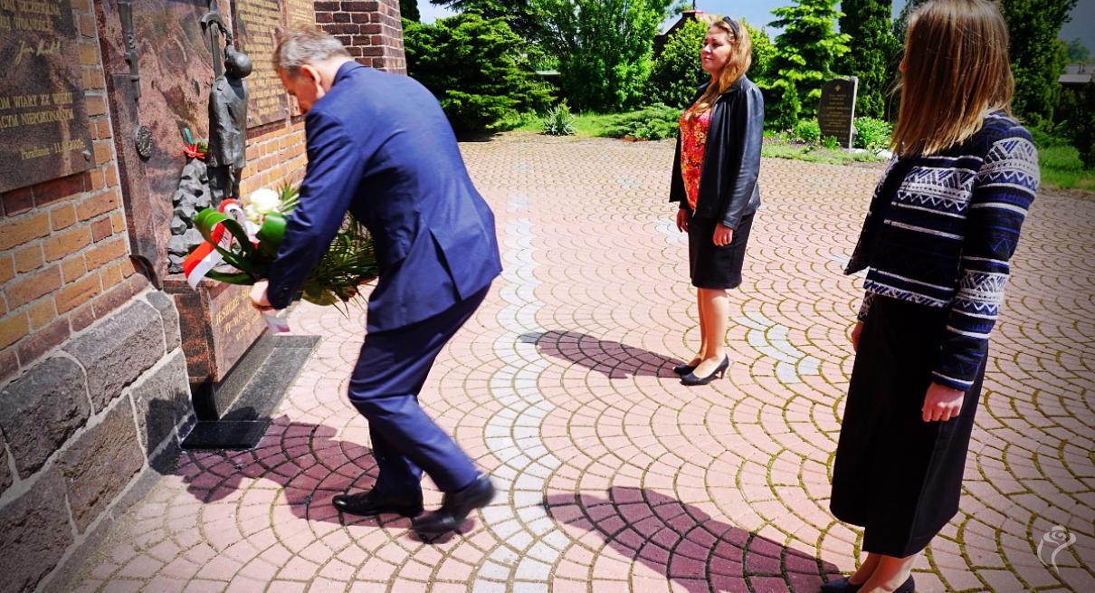 Na zdjęciu widać trzy osoby niosące kwiaty