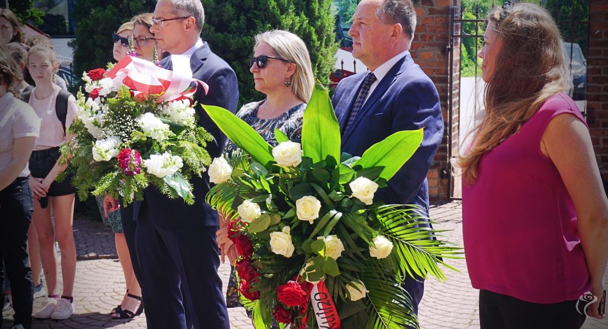 Na zdjęciu widać kilka osób, niektóre z nich trzymają kwiaty