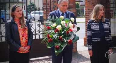 Na zdjęciu widać trzy osoby niosące kwiaty
