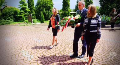 Na zdjęciu widać trzy osoby niosące kwiaty