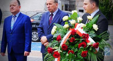 Na zdjęciu widać trzy osoby, jedna trzyma kwiaty