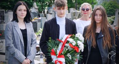 Na zdjęciu widać trzy osoby, jedna trzyma kwiaty