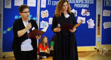 Na zdjęciu widać dwie kobiety mówiące do zgromadzonych