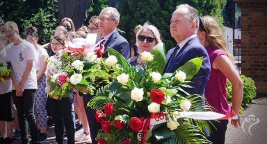 Na zdjęciu widać kilka osób, niektóre z nich trzymają kwiaty