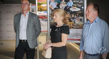 NA zdjęciu widać trzy osoby stojące przy wystawie